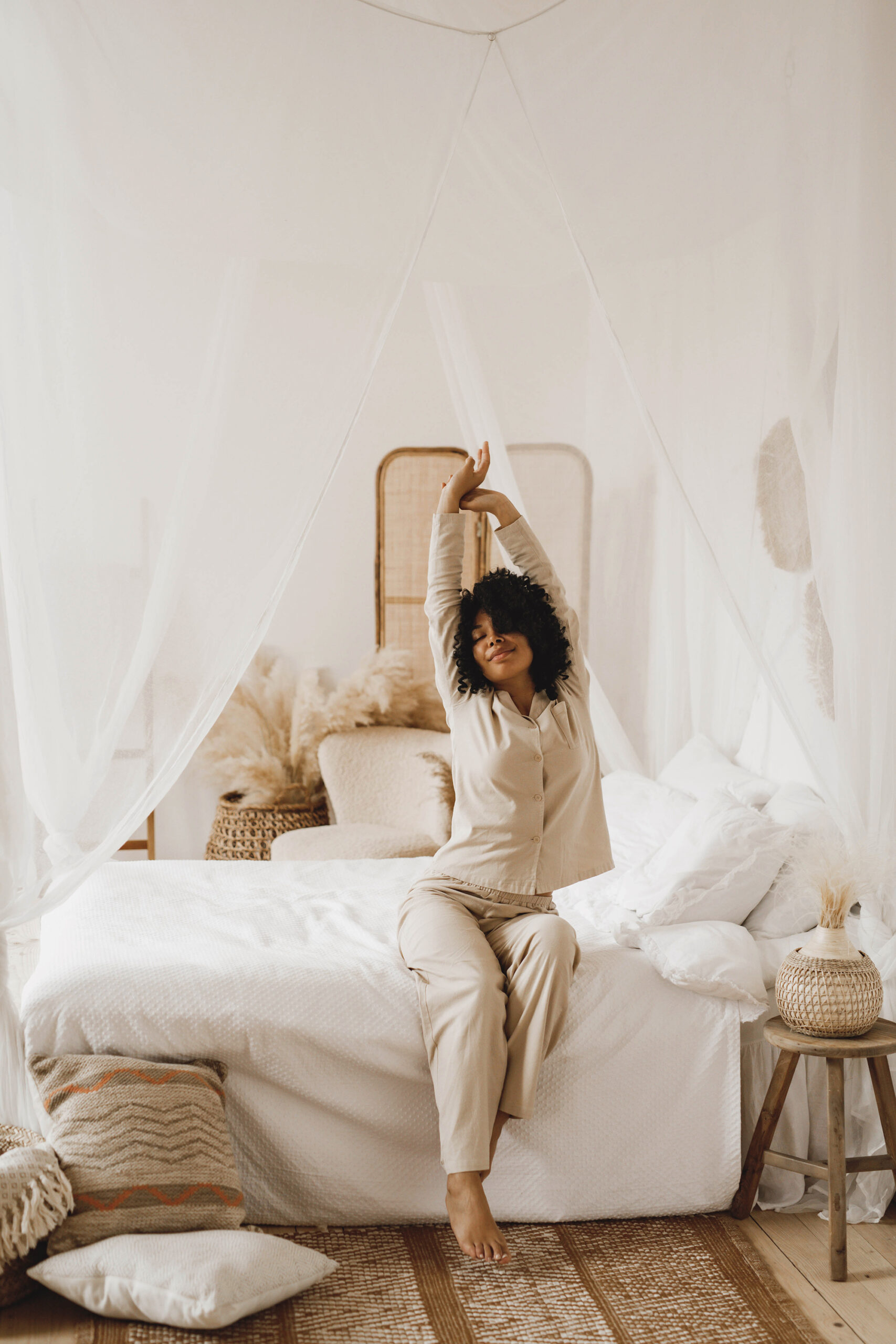 an image of a woman stretching while sitting on a bed on a blog post about postpartum sleep and helpful blankets