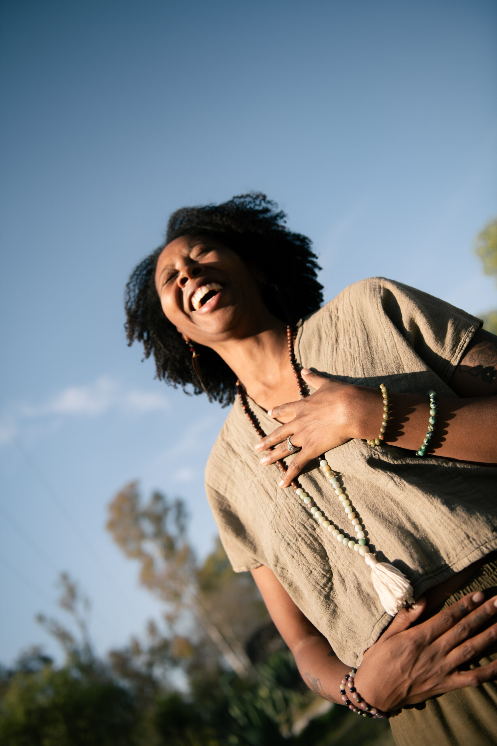 A Black woman laughing with her hands on her belly, embodying joy and ease in her body during the motherhood years